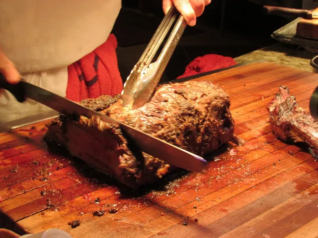 A person cutting meat on top of a wooden board.